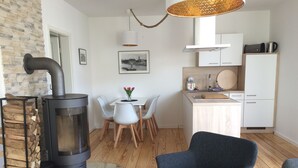 A compact living space with a wood-burning stove, a dining area with a white table and chairs, a kitchen with white cabinets, and a blue armchair.