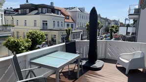 A rooftop terrace with a glass table, a black umbrella, and white chairs.