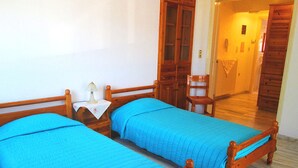 Una habitación con dos camas de madera, una mesita de noche con lámpara, una silla de madera y un armario de madera.