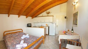 Un dormitorio con una cama, una mesita con una silla, una kitchenette y un baño.