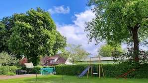 A backyard with a swing set, a slide, and a large tree. - Spacious apartment for up to 5 people centrally on the island of Rügen (Bergen auf Rügen OT Ramitz)