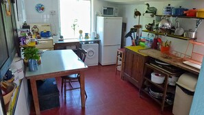Een kleine keuken met een wasmachine, een magnetron en diverse keukengerei op planken.