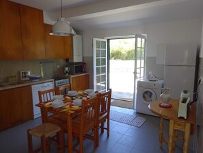Une cuisine avec des meubles en bois, une table à manger dressée avec de la vaisselle blanche, un four à micro-ondes, un lave-linge et une grande fenêtre.