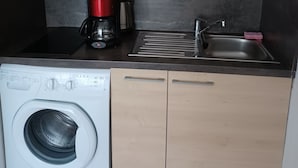 A compact kitchen with a washing machine, a coffee maker, and a sink.