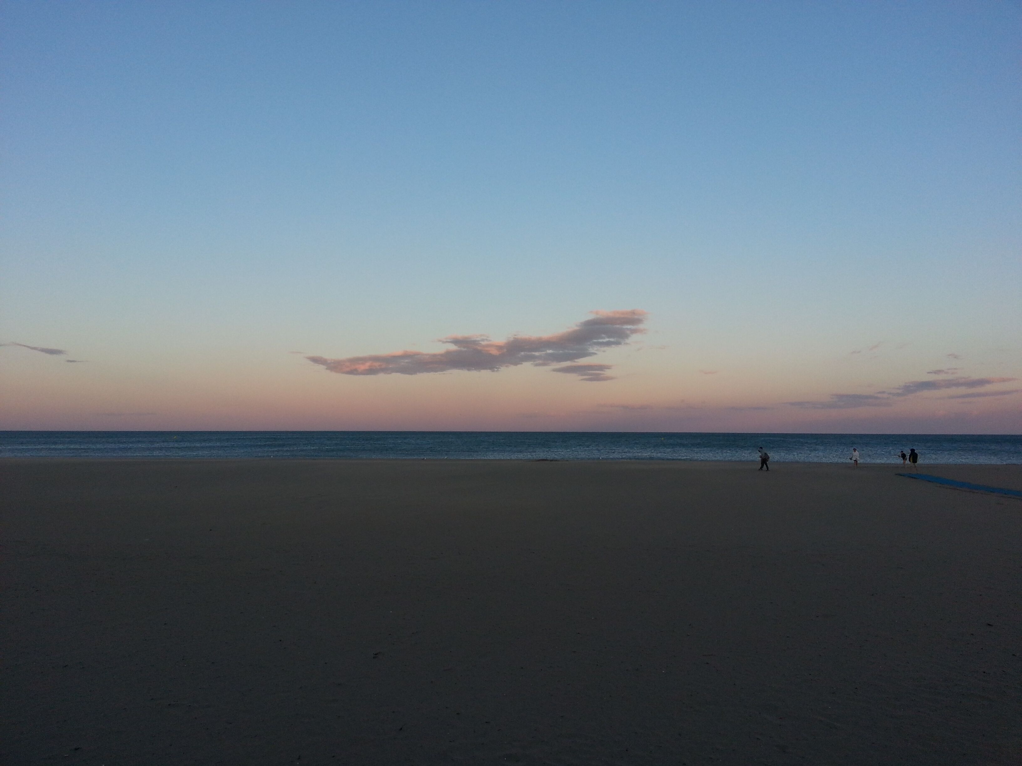 A wide beach with a clear sky and a few people in the distance.