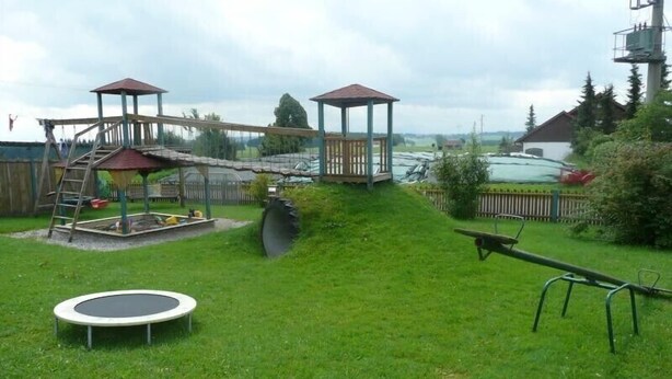 A playground with a seesaw, a trampoline, and a wooden climbing structure.