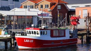 Ein rotes und weißes Boot mit dem Namen LAU-33 liegt in einer Marina an, mit Gebäuden im Hintergrund.