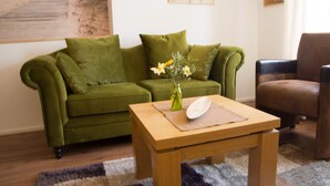 Ein grünes Sofa, ein Holztisch und ein brauner Ledersessel in einem Wohnzimmer.