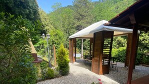 A covered outdoor seating area with a gravel path, surrounded by greenery and trees. - TV119: Cute vacation home for 4 people with private pool in the countryside (Camaiore)
