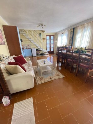 A living room with a sofa, coffee table, and dining area with chairs. A staircase is visible in the background. - TV119: Cute vacation home for 4 people with private pool in the countryside (Camaiore)