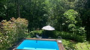 A rectangular swimming pool with a wooden deck, surrounded by lush greenery and trees. - TV119: Cute vacation home for 4 people with private pool in the countryside (Camaiore)