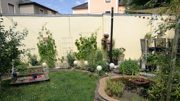A small, enclosed garden with a grassy area, a small pond, and various plants and decorations. - Spacious, close to the center and family friendly apartment in Dresden! (Dresden)