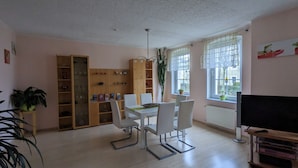 A dining area with a table and chairs, a bookshelf, a potted plant, and a television on a wooden stand. - Spacious, close to the center and family friendly apartment in Dresden! (Dresden)