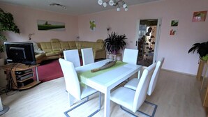 A dining area with a white table and chairs, a television in the background, and a plant on the right. - Spacious, close to the center and family friendly apartment in Dresden! (Dresden)