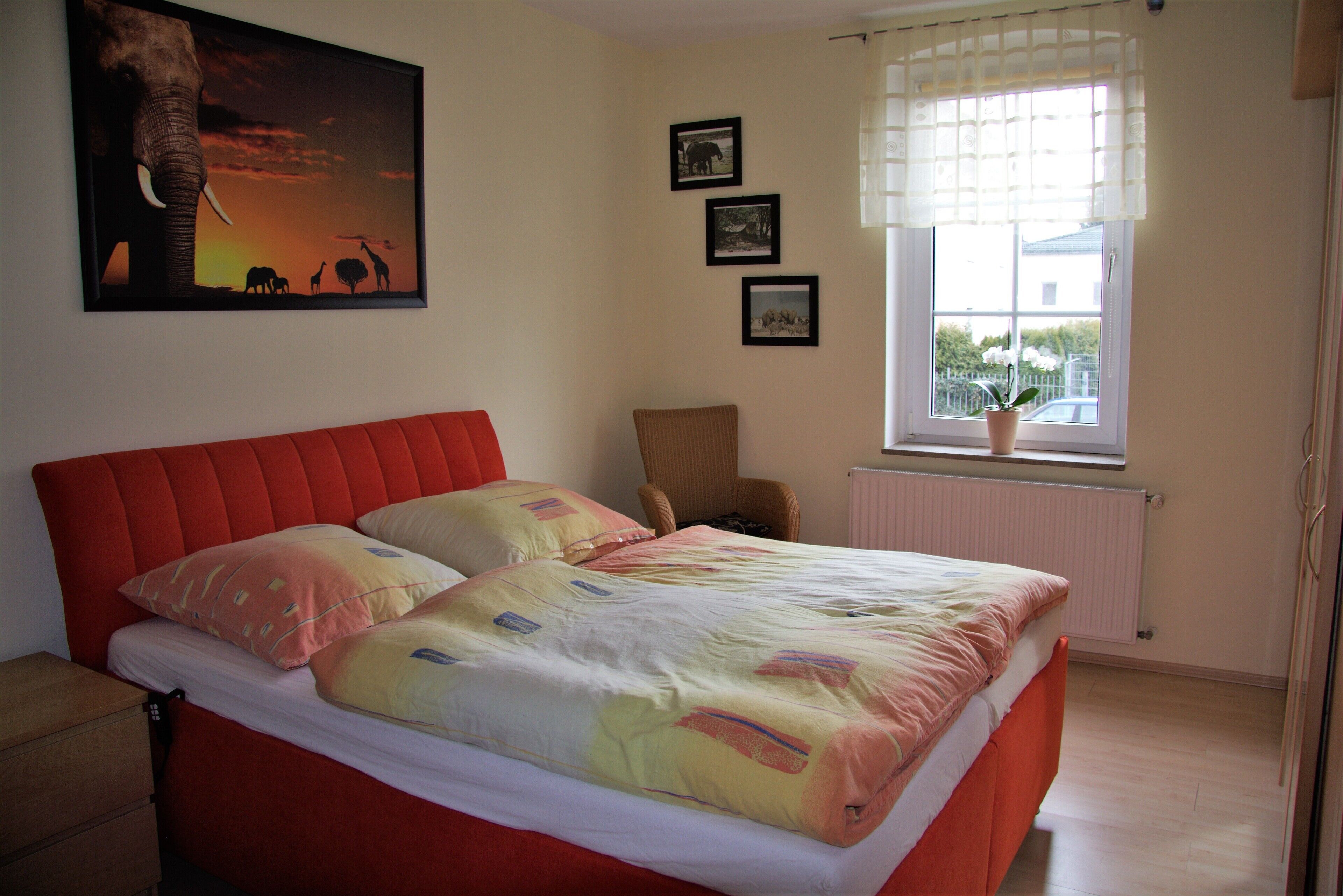 Ein Schlafzimmer mit einem roten Bett, einem Fenster mit Ausblick und einem gerahmten Bild an der Wand.