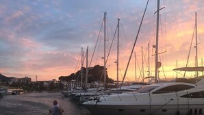 Satamassa on useita ankkuroituina olevia jahteja, ja laiturilla seisoo henkilö. Taustalla näkyy auringonlasku.