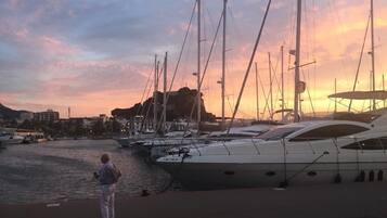 Een jachthaven met meerdere jachten die aanmeren, een persoon op de steiger, en een zonsondergang op de achtergrond.