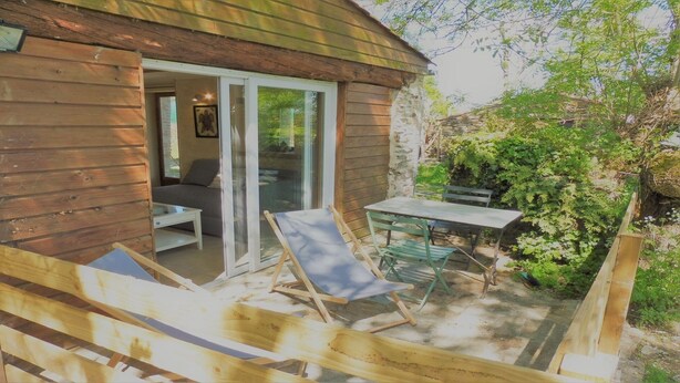 A wooden cabin with a sliding glass door leading to an outdoor seating area with a table and chairs. - Stopover 2, in the heart of the Vendée grove (saint florent des bois)