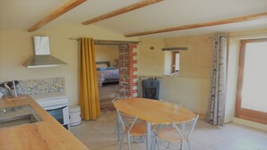 A kitchen with a dining table and chairs, a brick wall, and a window. - Stopover 2, in the heart of the Vendée grove (saint florent des bois)