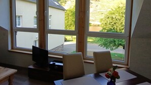 A room with a large window, a television on a wooden stand, two chairs, and a table with a vase of flowers. - Comfortable apartment, plus a balcony with stunning river view (Traben-Trarbach / Wolf)