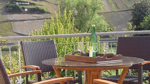A wooden deck with wicker furniture, a glass table, and a bottle. - Comfortable apartment, plus a balcony with stunning river view (Traben-Trarbach / Wolf)