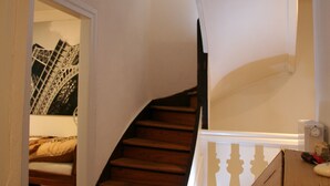 Una escalera de madera con barandilla blanca que lleva a una habitación con una cama y un reloj en la pared.