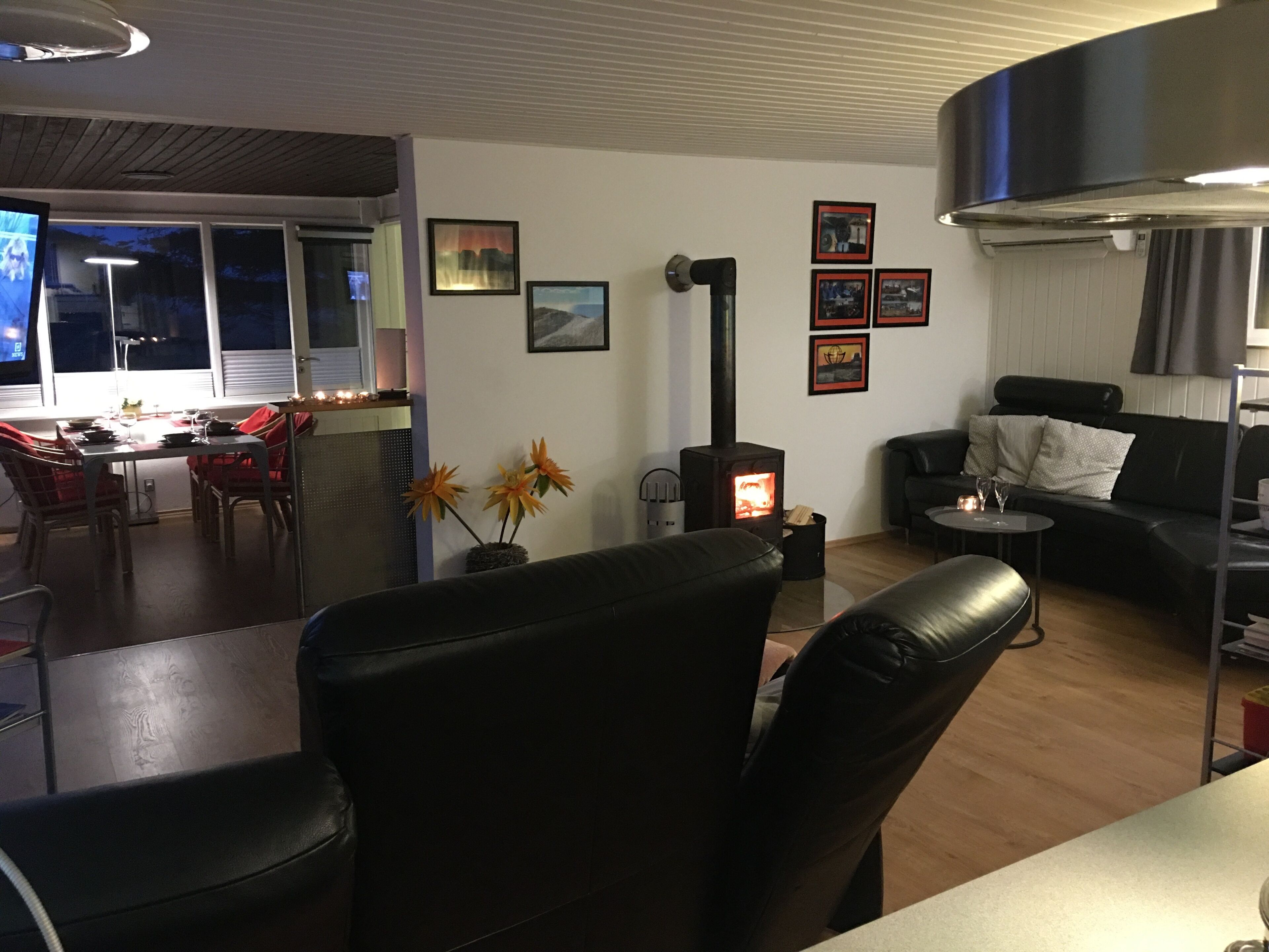 A modern living room with a fireplace, a dining area with red chairs, and a black leather sofa.