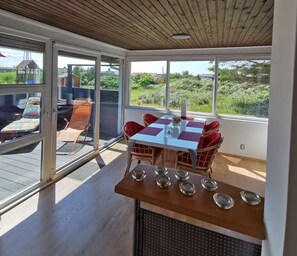 A sunlit room with a table and chairs, large windows, and a view of greenery outside. - Vacation home view LEUCHTTURM at the North Sea * Final cleaning 95€ on departure * (Hvide Sande)