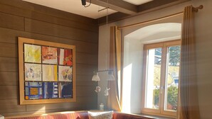 A dining area with a wooden table and benches, a large window with curtains, and a wall-mounted light fixture.