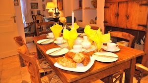 Una mesa de comedor dispuesta con platos, croissants y una vela, rodeada de sillas de madera.