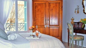 Un dormitorio con cama, cómoda, silla, ventana con contraventanas y puerta.