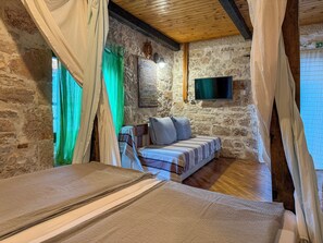 A rustic room with a stone wall, a bed with a striped blanket, a television mounted on the wall, and a wooden ceiling. - Time window, Mantova, Bed & Bike (Betina,Murter)