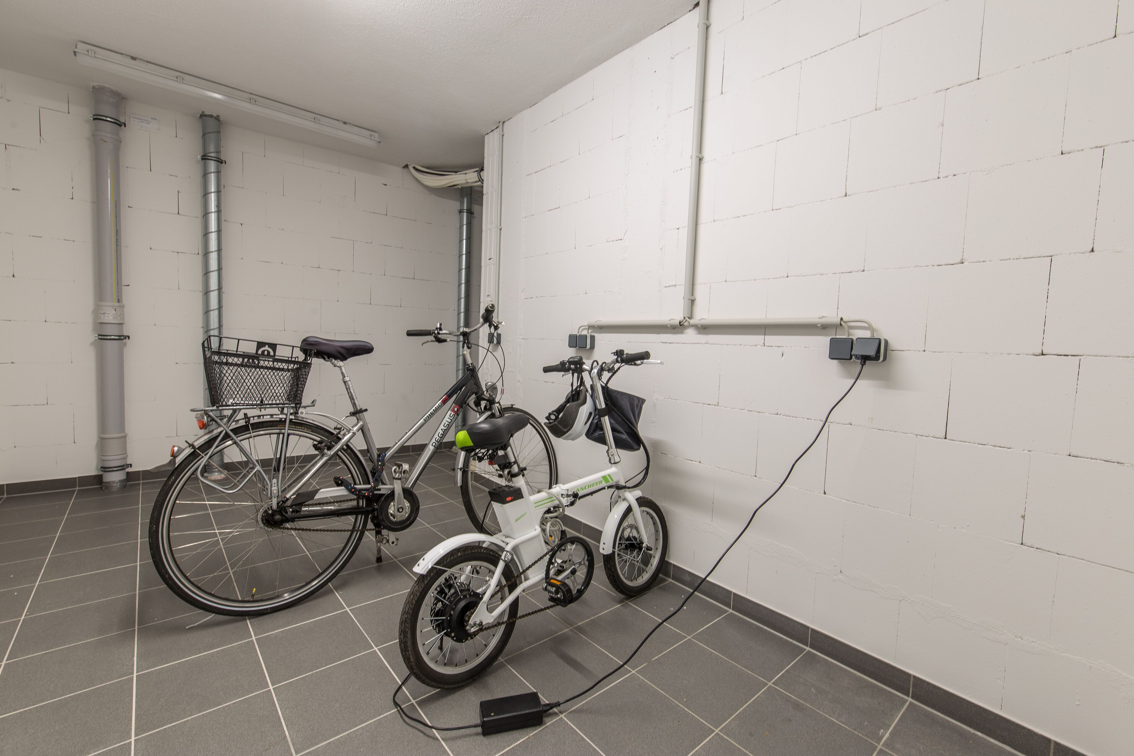 Une station de recharge pour vélos, située dans une pièce aux murs en briques blanches et au sol carrelé de couleur grise.