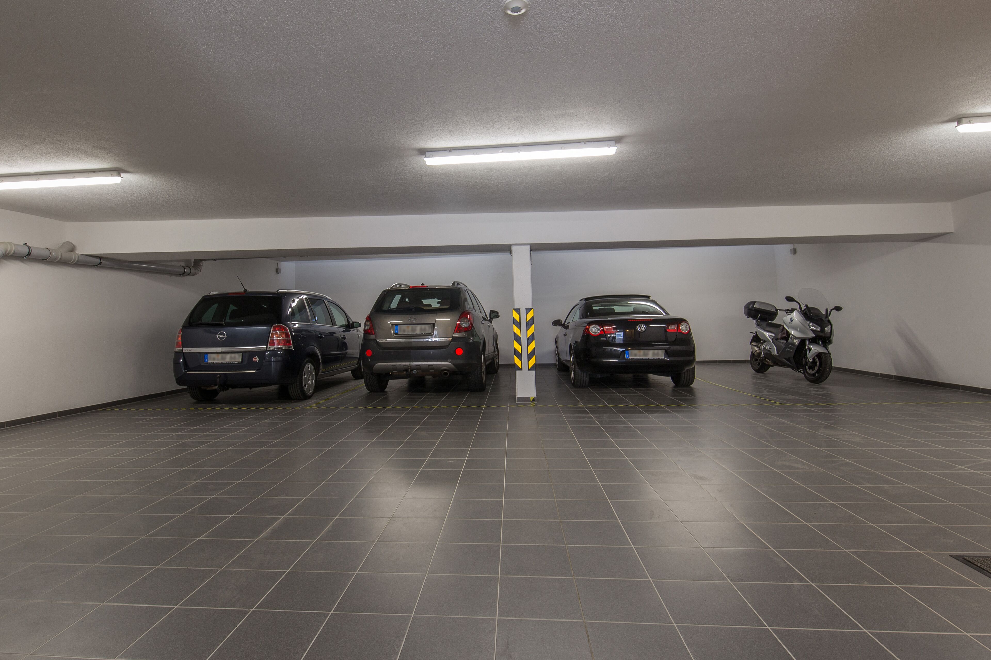 Un garaje para estacionar con tres coches y una motocicleta en fila.