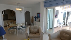 Ein Wohnzimmer mit Rattanmöbeln, einem Esstisch und Stühlen. Auf einem Tisch steht eine Vase mit Blumen.