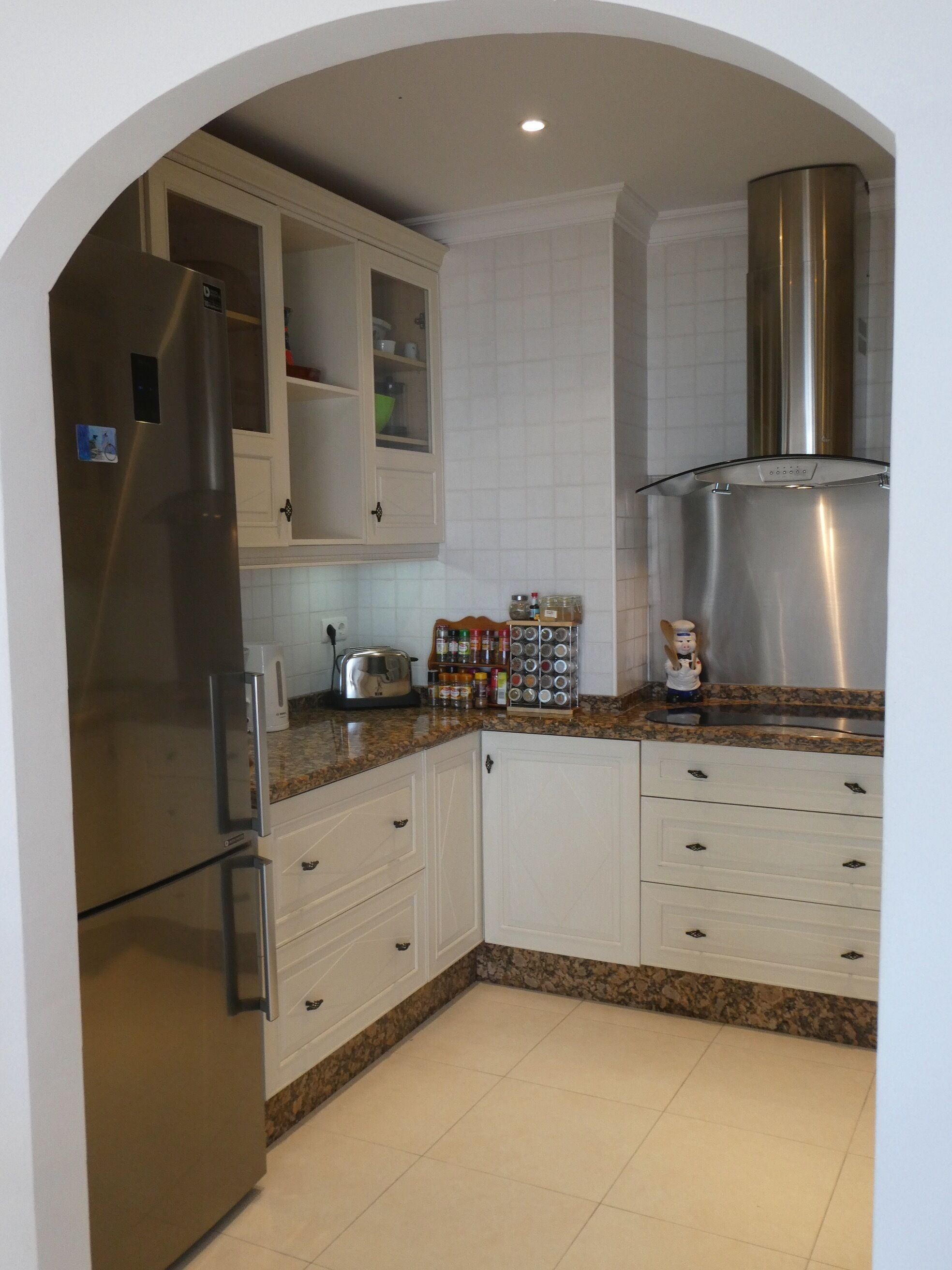 Eine Küche mit weißen Schränken, einem Edelstahl-Kühlschrank und einer Dunstabzugshaube.