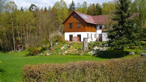 A two-story wooden house with a sloped roof, surrounded by a well-maintained garden and a dense forest in the background. - Holidays - Holidays in the Upper Palatinate low mountain range in Bavaria in the stone forest (Reuth bei Erbendorf)