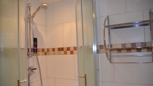 Une douche fermée par des parois en verre, dotée d’un pommeau et d’un flexible chromés, d’une porte en verre et d’un porte-serviettes chromé, le tout installé contre un mur carrelé.