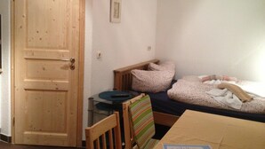 Une pièce avec une porte en bois, une petite table avec une télécommande, un lit avec une literie à motifs floraux et une chaise avec un coussin à rayures.