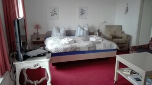 Quarto com cama, escrivaninha, cadeira e televisão.