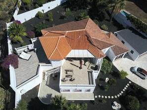 Vue aérienne d’une maison avec un toit en tuiles, une terrasse avec des meubles d’extérieur et une végétation luxuriante tout autour.