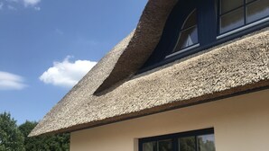 Una casa moderna con techo de paja, un ventanal grande y dos sillas de mimbre con cojines.