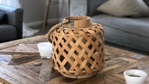 Una cesta de mimbre con un cierre metálico sobre una mesa de madera, una lámpara y un sofá con cojines en una sala de estar.