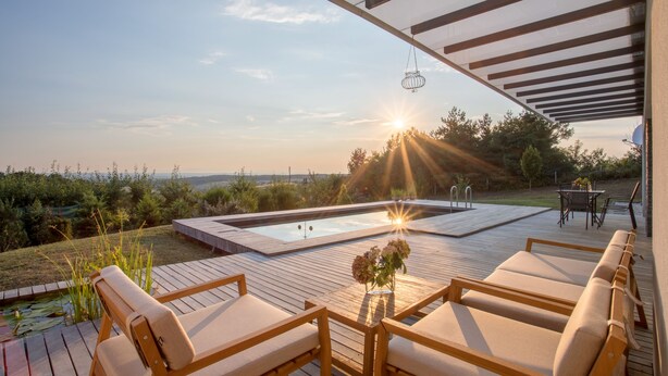 Eine Holzterrasse mit Liegestühlen und einem Whirlpool, mit Blick auf einen Garten und ein Gewässer.
