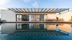 Ein modernes Haus mit Glasfassade, Pool und Gartenmöbeln.