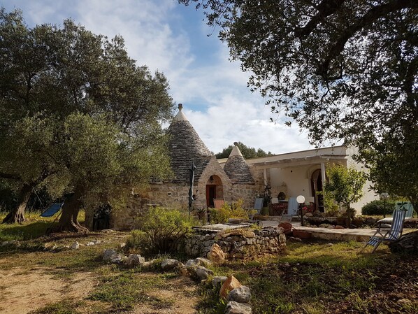 Un bâtiment rustique en pierre, doté d’un toit conique, entouré d’arbres et d’un jardin.