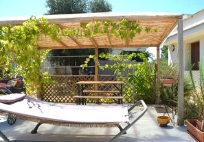 Un espace extérieur abrité, aménagé avec une table et des chaises, un hamac et une pergola couverte de plantes grimpantes.