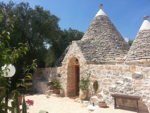 A stone building with a conical roof, a wooden door, and potted plants. - TRULLO in an evergreen olive grove in Salento, Apulia. (Ceglie Messapica)