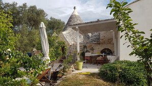 A stone house with a conical roof, a patio with outdoor seating, and lush greenery. - TRULLO in an evergreen olive grove in Salento, Apulia. (Ceglie Messapica)