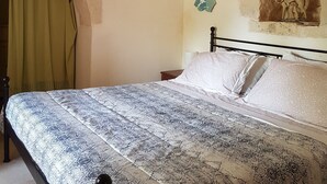 A bedroom with a stone wall, a bed with patterned bedding, a nightstand, and a green curtain. - TRULLO in an evergreen olive grove in Salento, Apulia. (Ceglie Messapica)